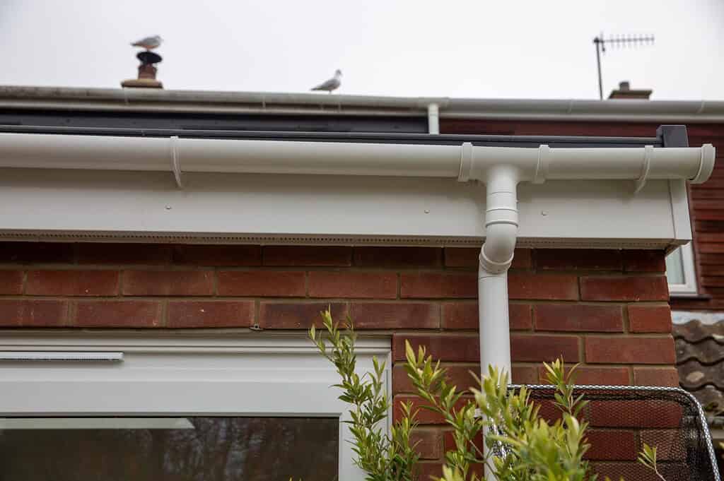 New white PVC guttering and downpipe installation on red brick house, expert roofing services.