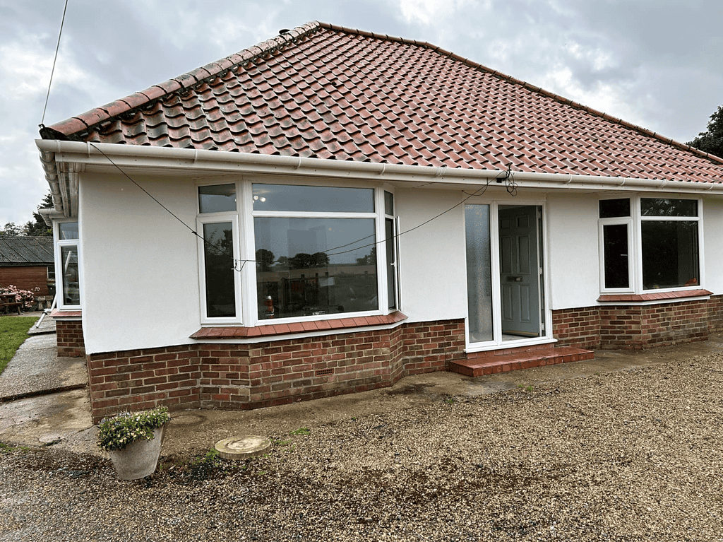 Bright modern house with white walls, red-tiled roof, large windows, and front garden, showcasing professional home renovation.