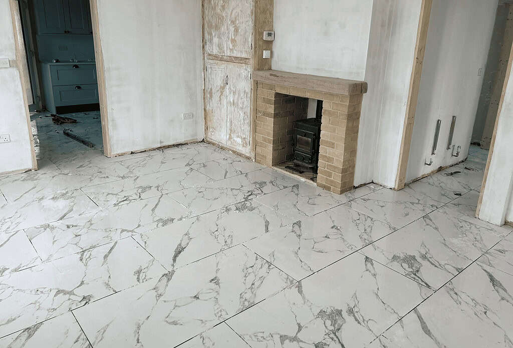 Marble effect tiled floor in under renovation living room with brick fireplace and unfinished walls.