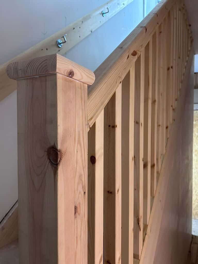 Natural wooden staircase handrail with balustrade in unfinished wood, indoor home renovation.